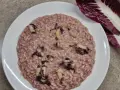 Un cremoso risotto al radicchio, con pezzetti di verdura che spuntano dal riso. Accanto, una foglia di radicchio fresco.