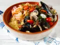 Un invitante cous cous di pesce, ricco di cozze, vongole, gamberi e pomodorini, guarnito con prezzemolo fresco.