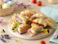 Delizioso antipasto di Pasqua con croissant farciti, uova colorate in un cesto e fiori primaverili.