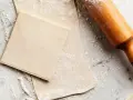 Farinata e mattarello su piano di marmo, pronti per creare pasta sfoglia fatta in casa.