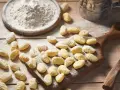 Gnocchi senza glutine appena fatti, spolverati di farina, su un tagliere di legno.