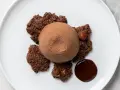 Semifreddo al cioccolato su croccanti biscotti al cacao, con una nocciola intera e una goccia di salsa al cioccolato.