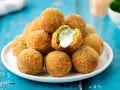 Pile di polpette di broccoli dorate e croccanti, una con il cuore filante di formaggio.
