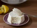 Ricotta fatta in casa su un piatto viola, con limone tagliato a metà sullo sfondo. Un cucchiaino preleva una porzione cremosa.