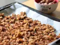 Granola fatta in casa appena sfornata su carta da forno, con una ciotola di frutta secca sullo sfondo.