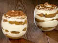 Due bicchieri di delizioso tiramisù senza uova, con strati di savoiardi e crema, spolverati di cacao.