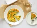 Deliziosa frittata di asparagi al forno, servita su un piatto bianco con una fetta a parte e un bicchiere di vino.