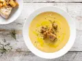 Una cremosa vellutata di ceci, guarnita con crostini dorati, olio d'oliva e rosmarino fresco, su un tavolo di legno rustico.