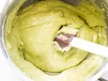 Una spatola mescola una densa crema al pistacchio in una ciotola d'acciaio.