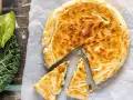 Torta salata con pasta sfoglia dorata, ripiena di verdure. Accanto, foglie di cavolo nero fresco.