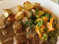 Un saporito spezzatino con piselli, carote e patate arrosto, guarnito con prezzemolo fresco.