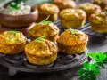 Tortini di zucchine dorati e fragranti, guarniti con rosmarino, su un piatto di ghisa. Sullo sfondo, una ciotola di formaggio fresco.
