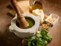 Mortaiolo in marmo con pestello in legno, basilico fresco, pinoli, noci, aglio, parmigiano e olio d'oliva, ingredienti per un autentico pesto di basilico.