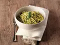Un piatto invitante di trofie al pesto, guarnito con una foglia di basilico, su un tavolo di legno rustico.