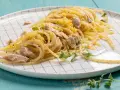 Un piatto di pasta tonno e limone, condita con scorza di limone grattugiata e erbe aromatiche fresche, servita su un piatto a scacchi bianchi.