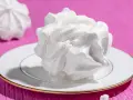 Dolci meringhe bianche, perfette per le tue ricette con albumi, su un piatto con bordo dorato, su sfondo fucsia.