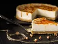 Una fetta di cheesecake senza panna, con glassa caramellata, su un piatto da portata. Sullo sfondo, la torta intera.