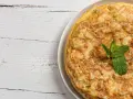 Frittata di cipolle dorata e soffice, guarnita con foglie di menta fresca, su un tavolo di legno bianco.