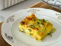 Una fetta di lasagne di verdure, con piselli e carote, su un piatto bianco decorato.