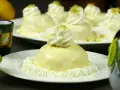 Dolcetti rotondi con glassa al limone e panna montata, guarniti con scorza di limone. Sullo sfondo, limoni freschi e bicchierini decorati.