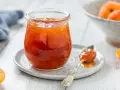 Vasetto di marmellata di albicocche, con un cucchiaino carico e albicocche fresche sullo sfondo.