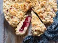 Torta con marmellata, con crosta friabile e ripieno rosso brillante. Una fetta mostra la consistenza succosa.