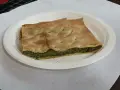 Una fetta di torta pasqualina originale genovese, con pasta sfoglia dorata e ripieno verde di spinaci e ricotta, servita su un piatto bianco.