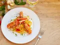 Un piatto di linguine agli scampi, condite con pomodorini e prezzemolo, accompagnato da ingredienti freschi e un bicchiere di vino bianco.