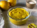 Crema pasticcera senza uova, densa e vellutata, in una ciotola di vetro. Limoni e zucchero sullo sfondo, pronti per un dolce delizioso.