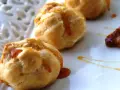 Bignè alla crema soffici e dorati, bagnati da un filo di caramello lucido su un piatto bianco.