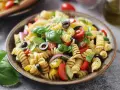 Un piatto invitante di insalata di pasta con fusilli, pomodorini, olive nere, cipolla rossa, cetrioli e basilico fresco.