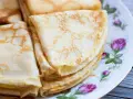 Deliziose crepes senza latte, piegate e impilate su un piatto decorato con rose. Perfette per una colazione leggera o uno spuntino.