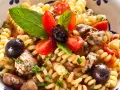 Pasta con pesce spada, pomodorini, olive nere e menta fresca in una ciotola decorata. Un piatto estivo che profuma di mare.