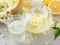 Un bicchiere e una caraffa di sciroppo di sambuco ricetta, con fiori di sambuco freschi e fette di limone.