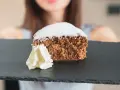Una fetta di pan di spagna al cacao, soffice e spolverata di zucchero a velo, servita con panna montata su una lavagna scura.