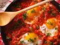 Uova al pomodoro cotte in padella, con tuorli dorati e prezzemolo fresco. Un cucchiaio di legno attende di servire questo piatto saporito.