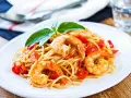 Un piatto invitante di spaghetti con gamberetti succulenti e pomodorini freschi, guarnito con basilico.
