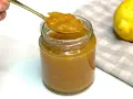 Un cucchiaio d'oro raccoglie la densa marmellata di limoni da un barattolo di vetro. Due limoni freschi riposano su un tovagliolo a quadretti.