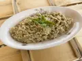 Crema di melanzane rustica, guarnita con basilico fresco, servita in un piatto ovale su un tavolo di legno grezzo.
