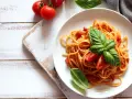 Spaghetti al sugo di pomodoro fresco, guarniti con basilico e pomodorini, su un piatto bianco.