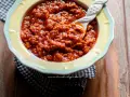 Un invitante sugo con salsiccia, denso e saporito, servito in una ciotola gialla con un cucchiaio decorato.
