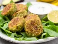 Deliziose polpette di spinaci dorate, servite su un letto di spinacini freschi con salsa e spicchi di lime.