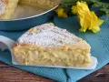 Una fetta di pastiera napoletana con crema pasticcera, cosparsa di zucchero a velo, su un piatto bianco, con fiori gialli sullo sfondo.