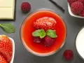 Un bicchiere di coulis di fragole con fragola, lamponi e menta. Accanto, fragole fresche, cioccolato bianco, lamponi e un bicchiere di latte.