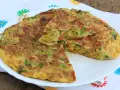 Frittata con fiori di zucca, carote e olive, tagliata a spicchi su un piatto bianco, con un tovagliolo fiorato sullo sfondo.