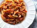 Piatto di pasta alla boscaiola con penne, funghi, salsiccia e pomodoro, condita con prezzemolo fresco.