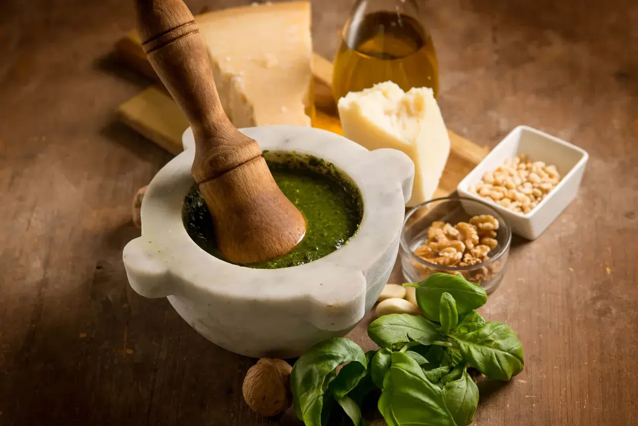 Mortaiolo in marmo con pestello in legno, basilico fresco, pinoli, noci, aglio, parmigiano e olio d'oliva, ingredienti per un autentico pesto di basilico.