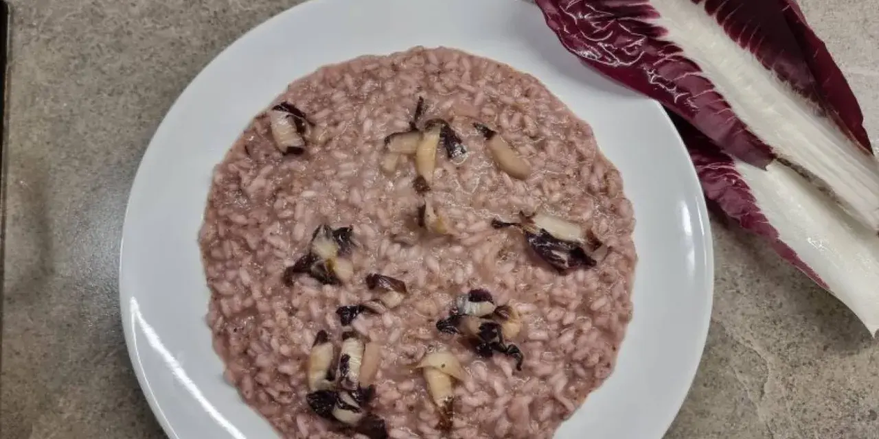 Un cremoso risotto al radicchio, con pezzetti di verdura che spuntano dal riso. Accanto, una foglia di radicchio fresco.