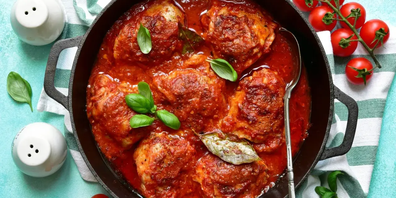 Pollo in umido succulento in padella con pomodoro e basilico, pronto per essere gustato.