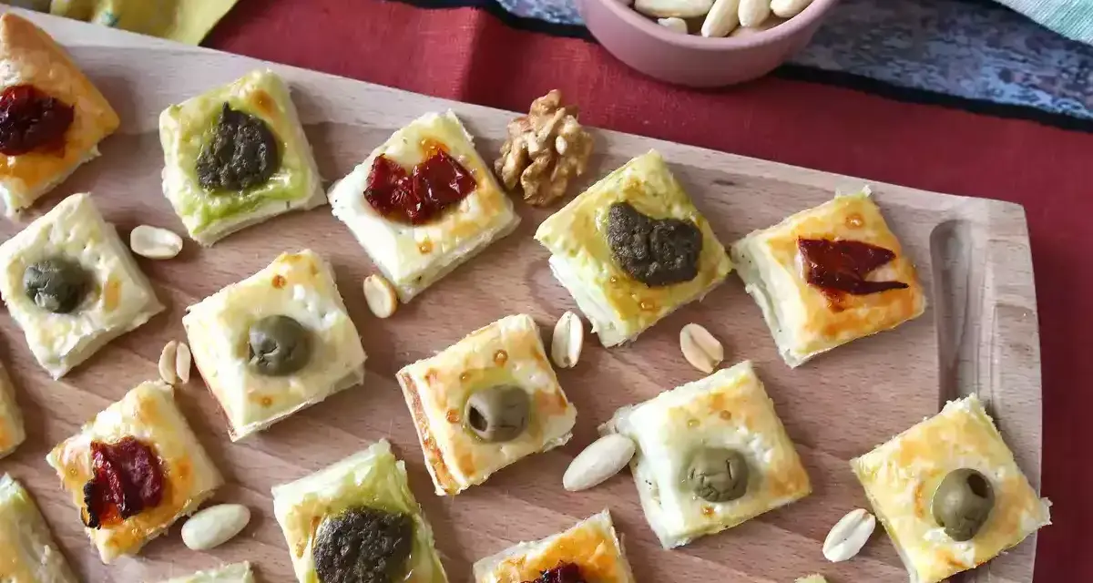 Sfiziose ricette con pasta sfoglia: quadratini dorati con olive, pesto e pomodori secchi, perfetti per un aperitivo.